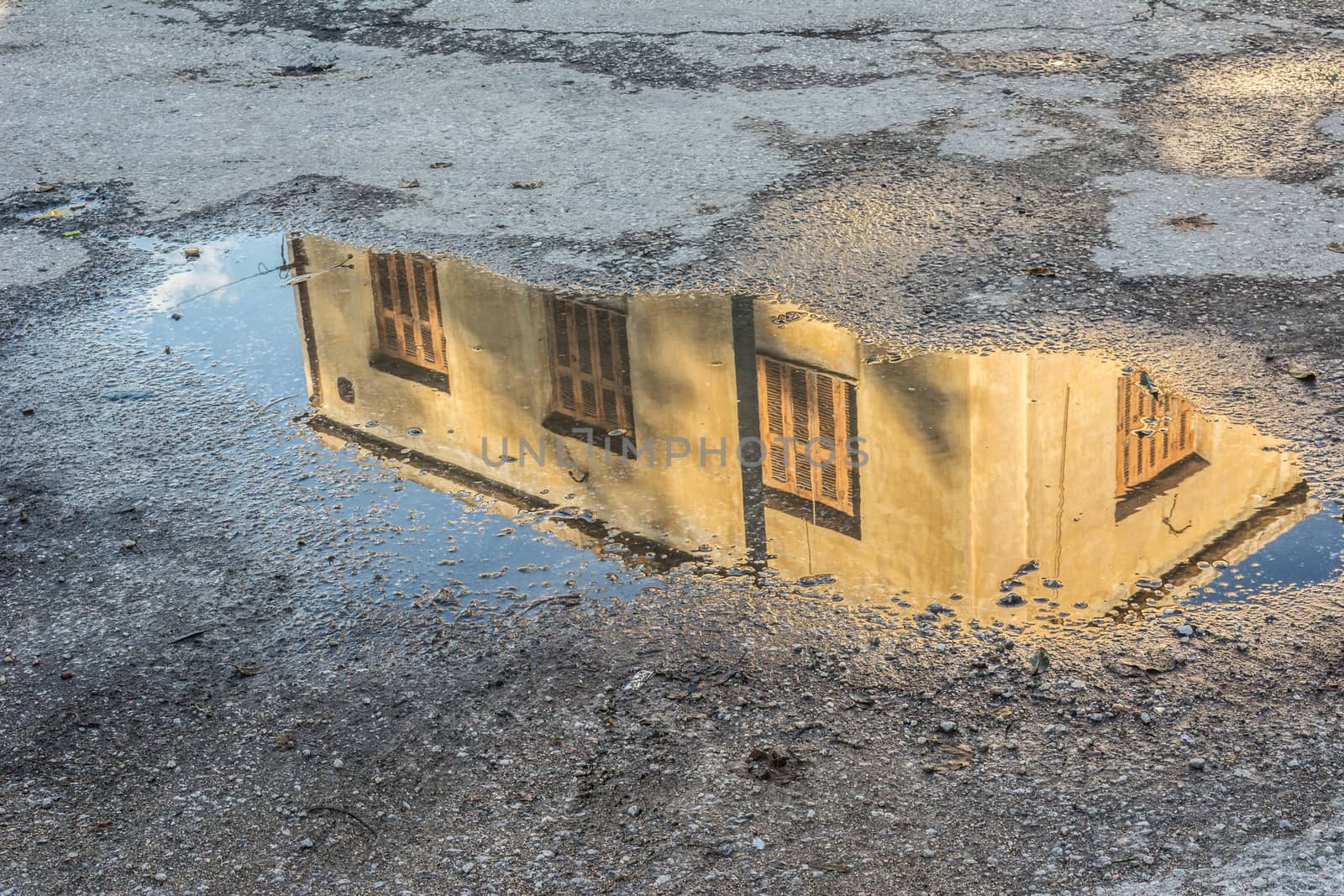Abandoned building with yellow shutters reflects in a puddle after rain in Athens, Greece