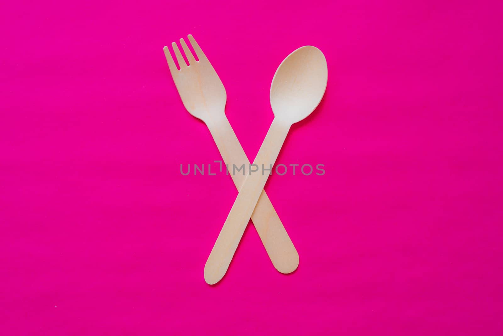 Wooden fork and spoon on a strong pink colour background, concept studio photo