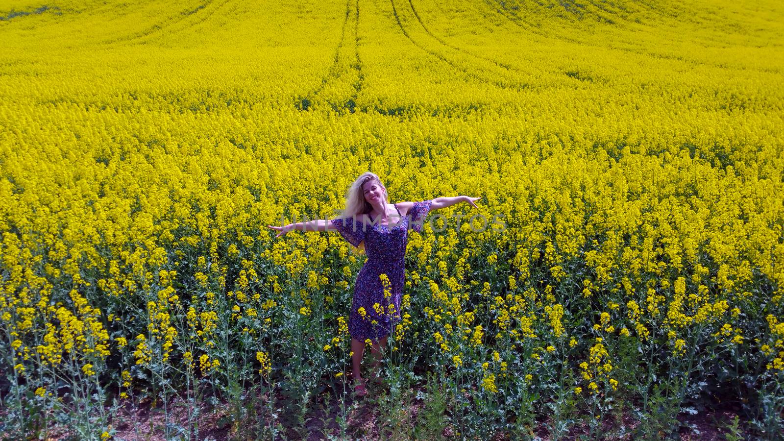 happy blonde girl in dress with flower print on the blooming yellow rapeseed field