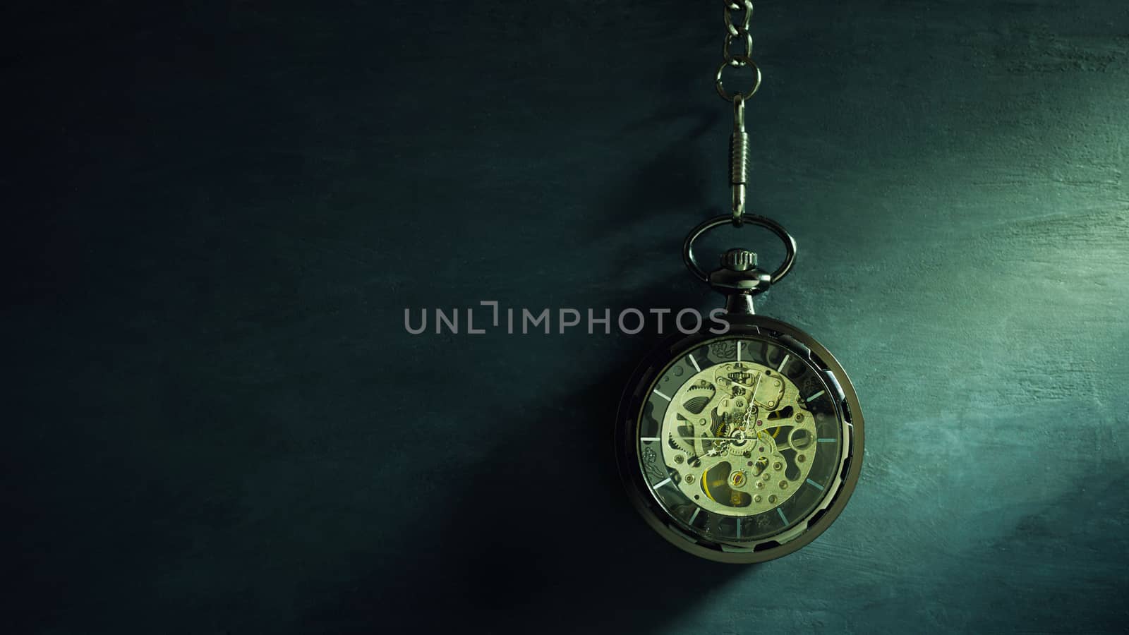 Pocket watch hanging on black chalkboard and sunlight in morning. Concept of time and education.