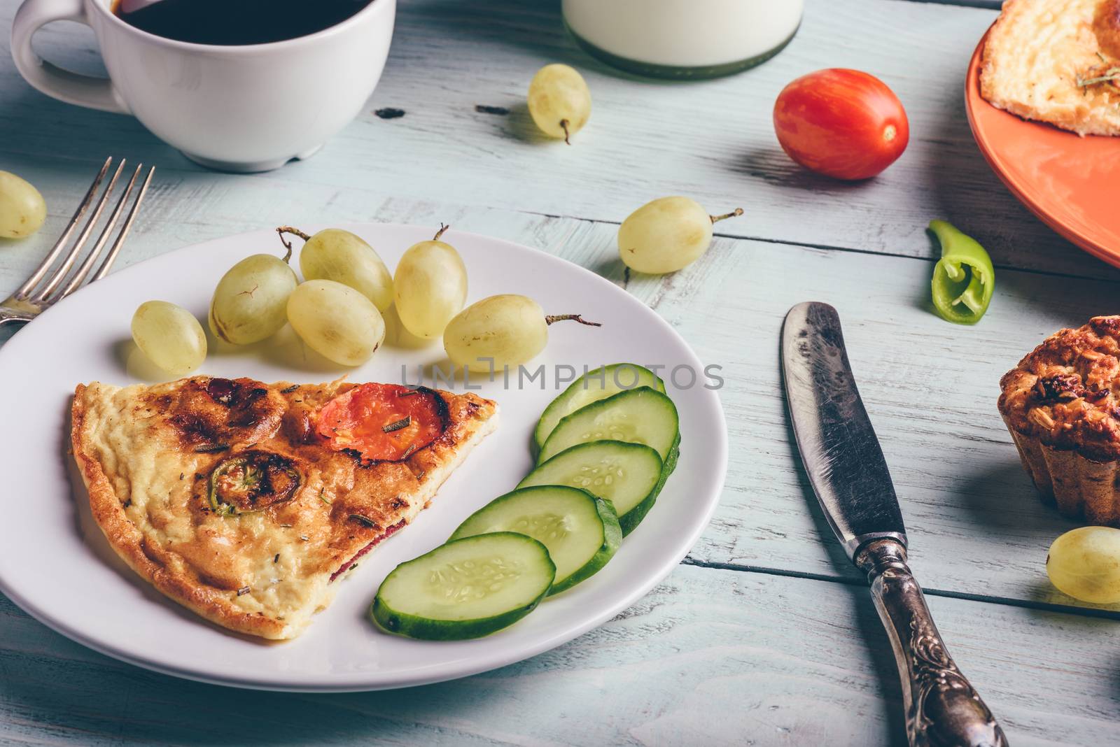Slice of frittata with cup of coffee, grapes and muffins over light wooden background. Healthy eating concept.