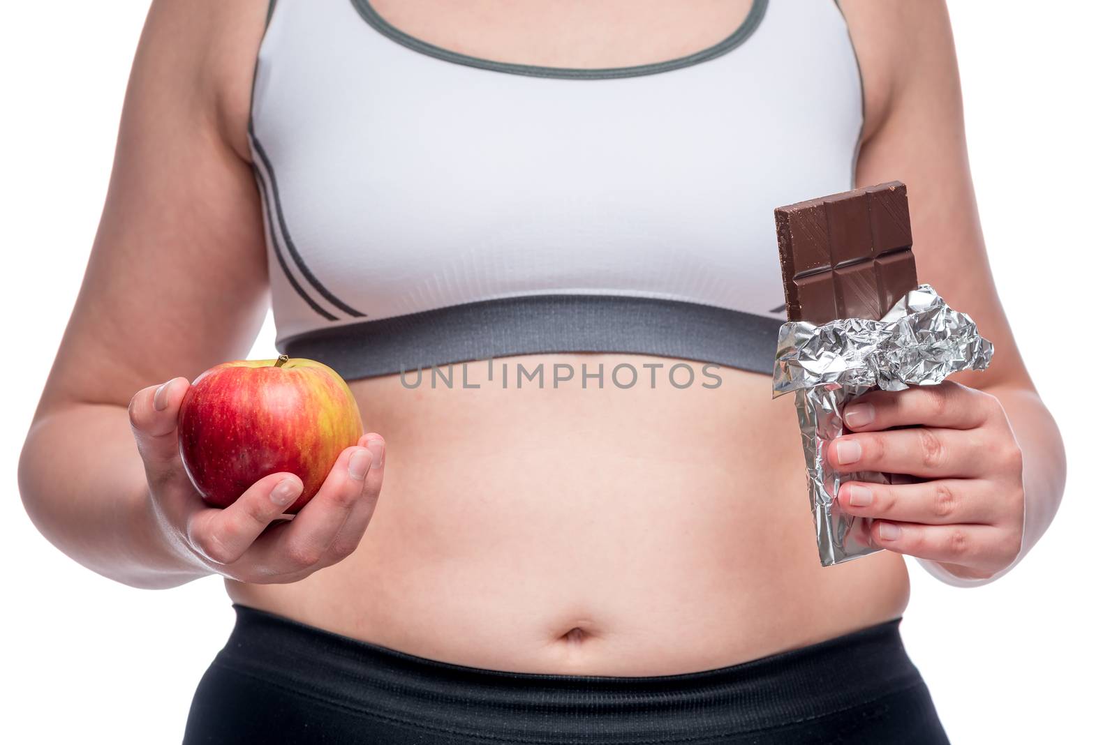 Fat woman makes a difficult choice between an apple and chocolate, in the frame a close-up belly