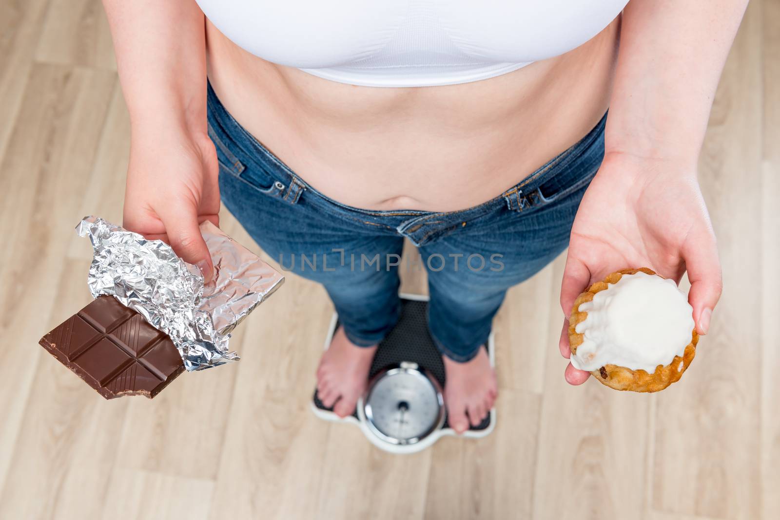 woman weighs on scales, chocolate in her hands and donut