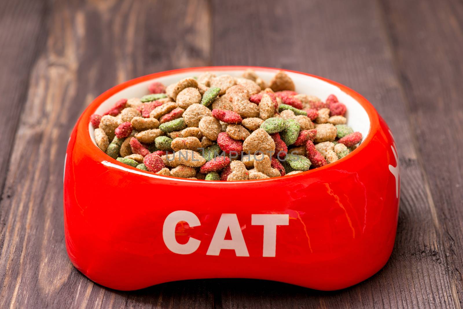 close-up red cat bowl with dry food on the floor at home by kosmsos111