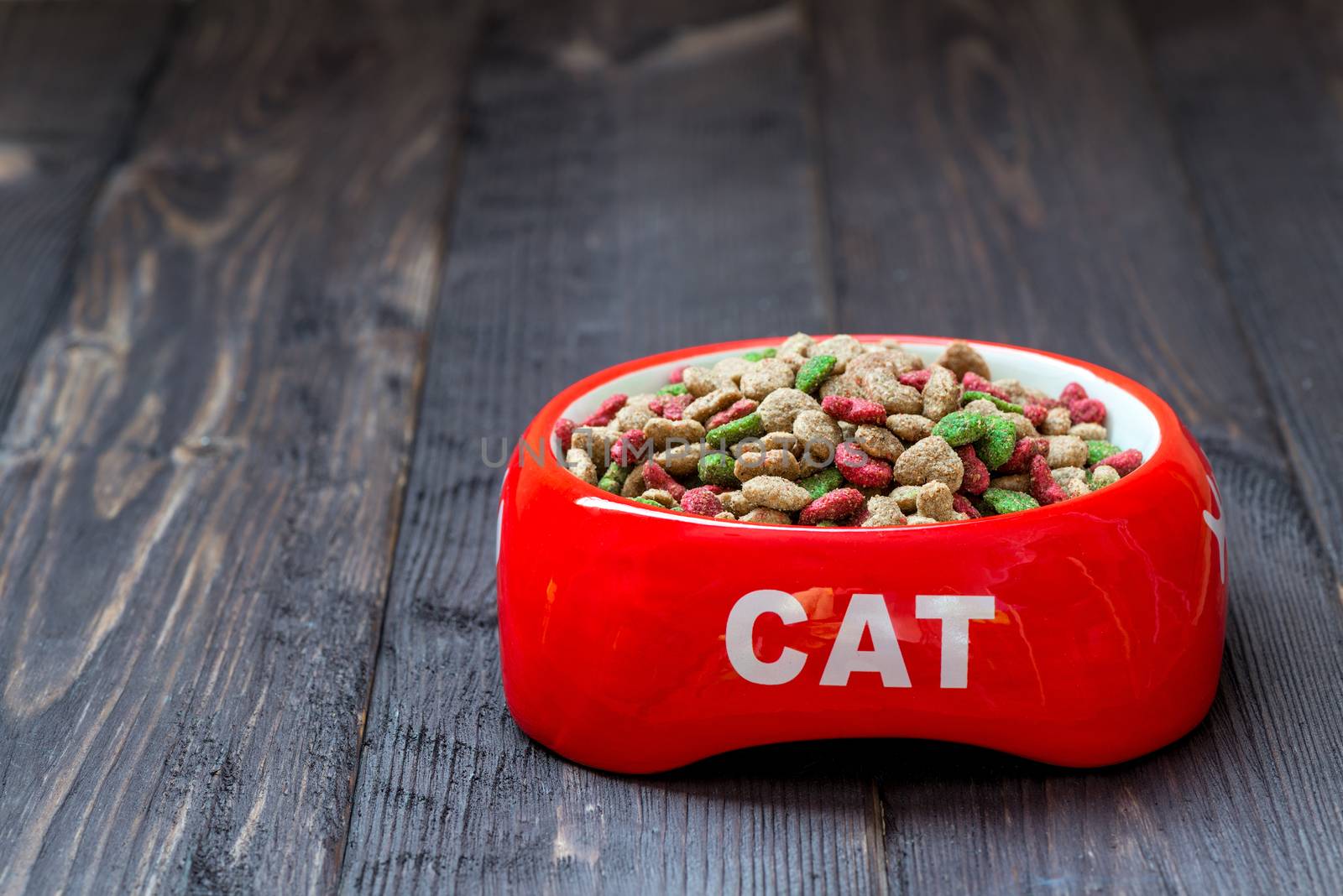 on a wooden floor a red bowl for a cat with dry food