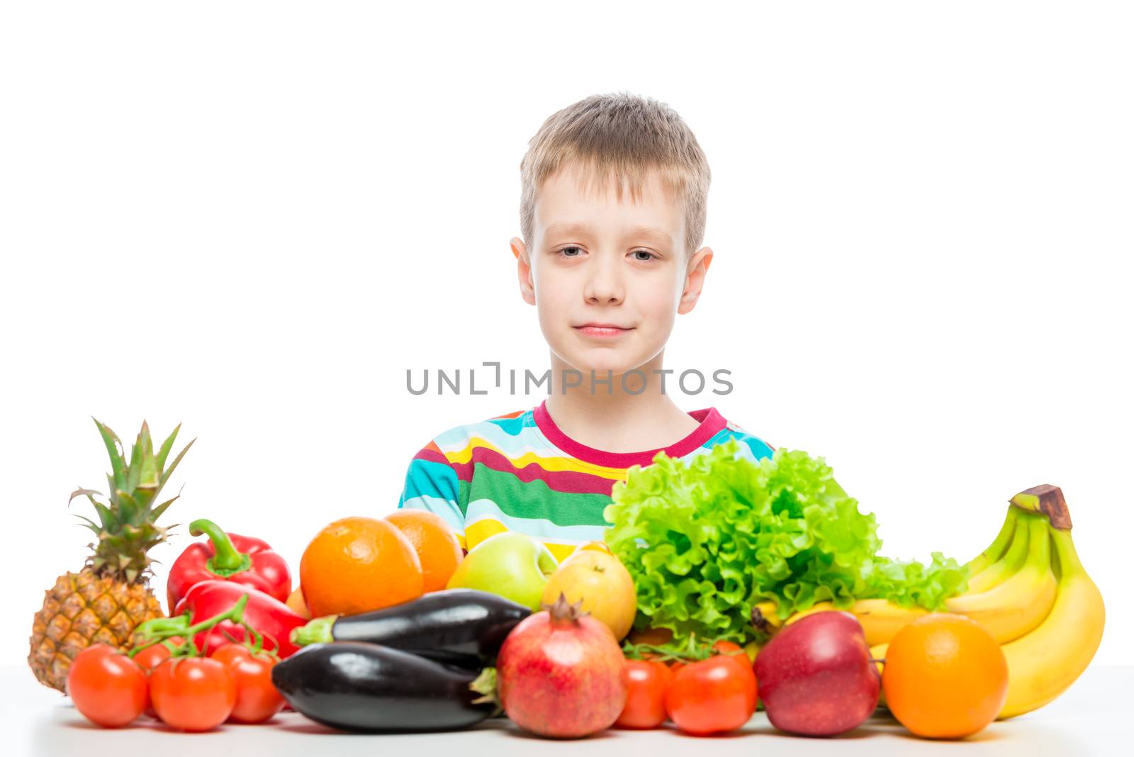 Portrait of a boy at the table with a pile of fresh vegetables and fruits isolated in studio