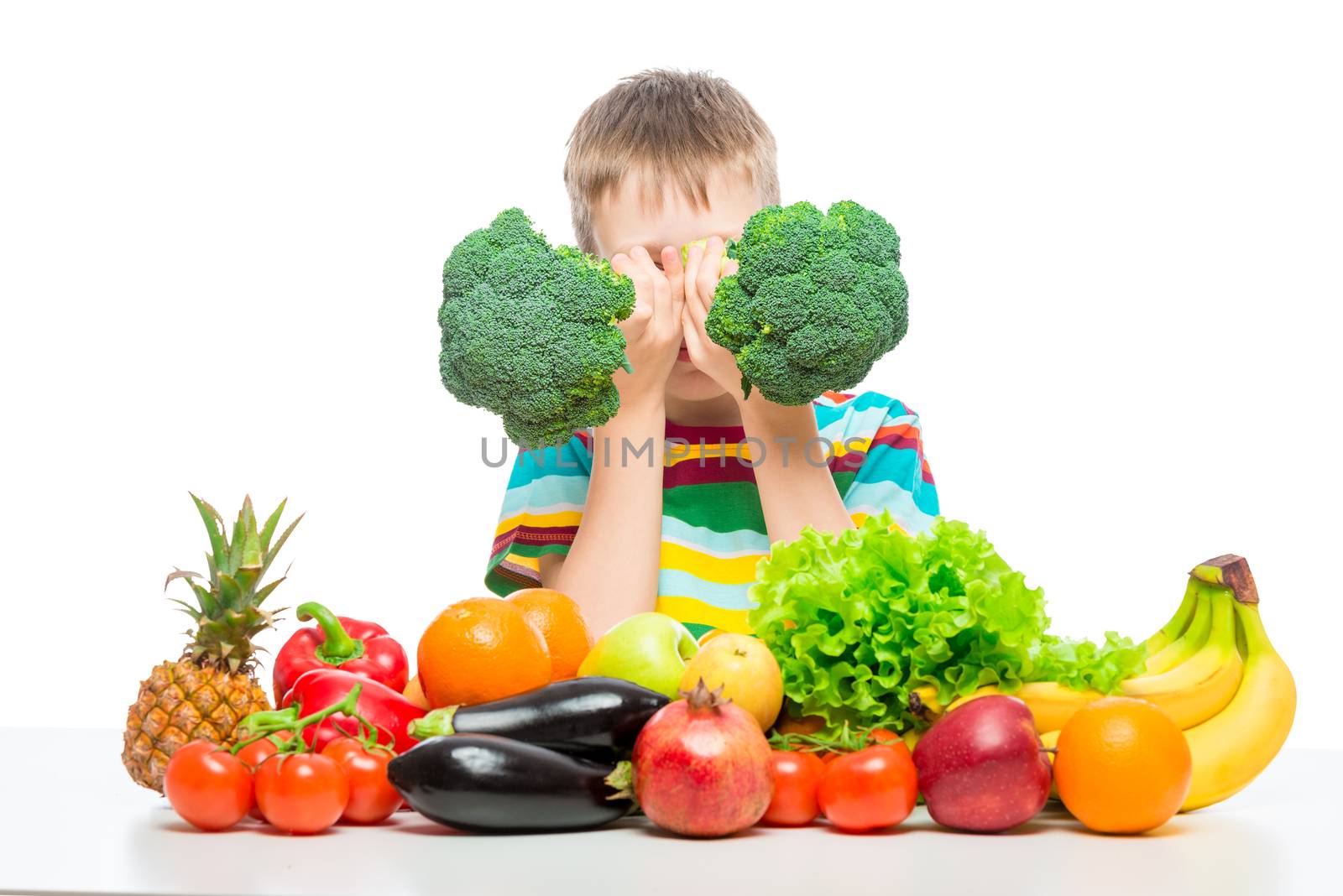 Boy playing with broccoli and a bunch of vegetables and fruits posing in the studio isolated on white background