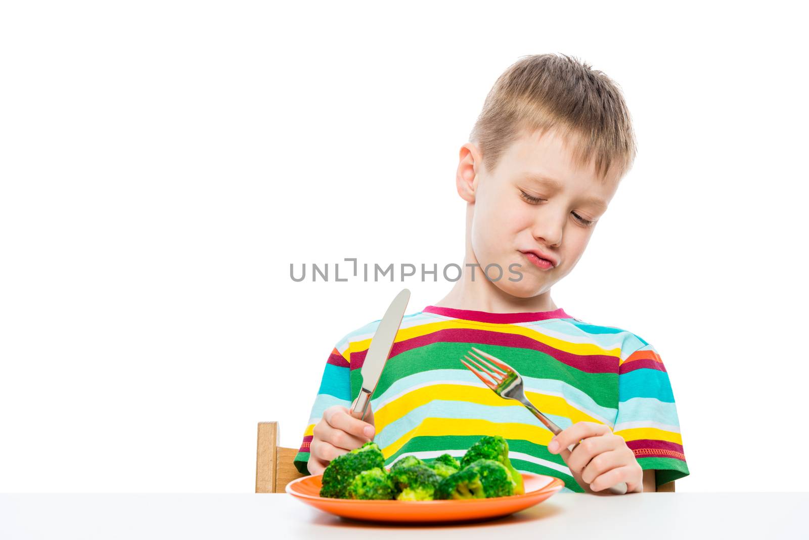 A boy of 10 years old looks at broccoli in a plate in disgust, portrait is isolated on a white background