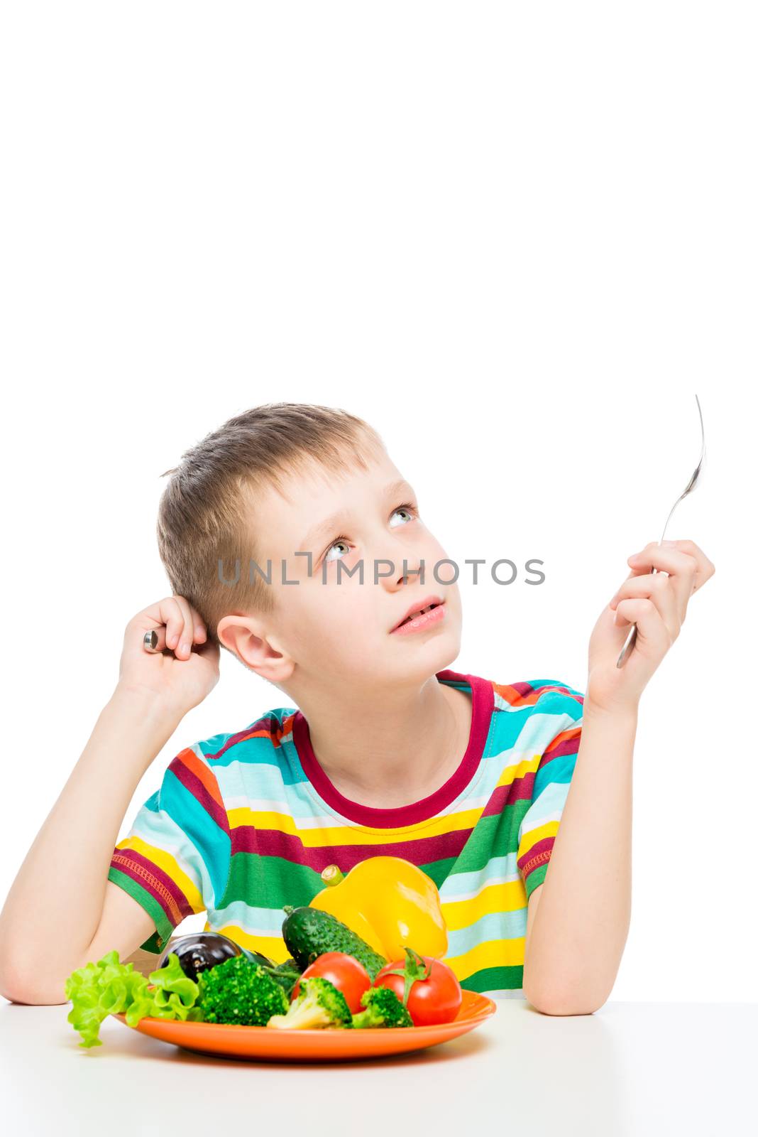 portrait of a boy at the table with a plate of vegetables for lunch, isolated on white background