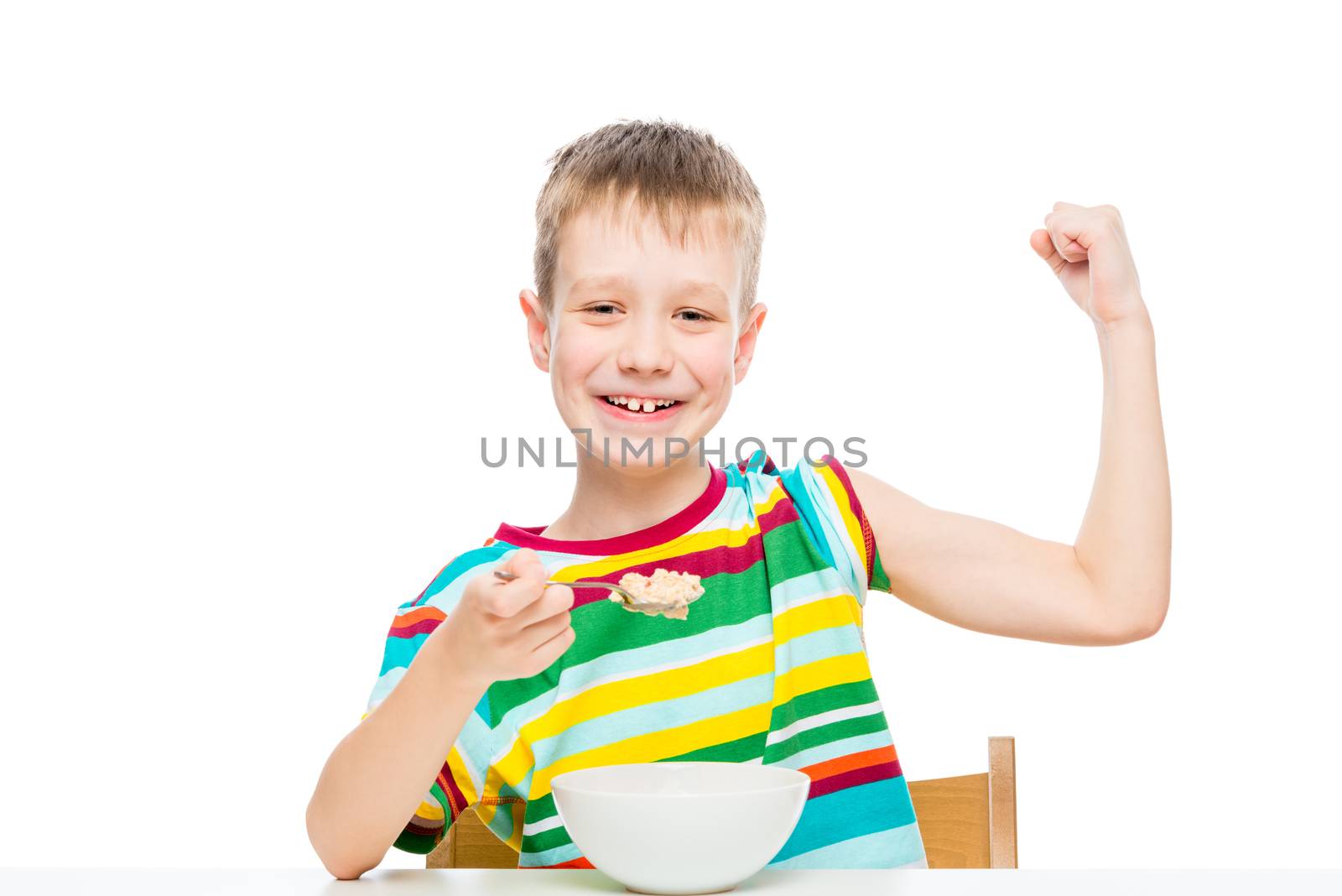 concept - proper nutrition, a strong healthy boy shows biceps, eats porridge