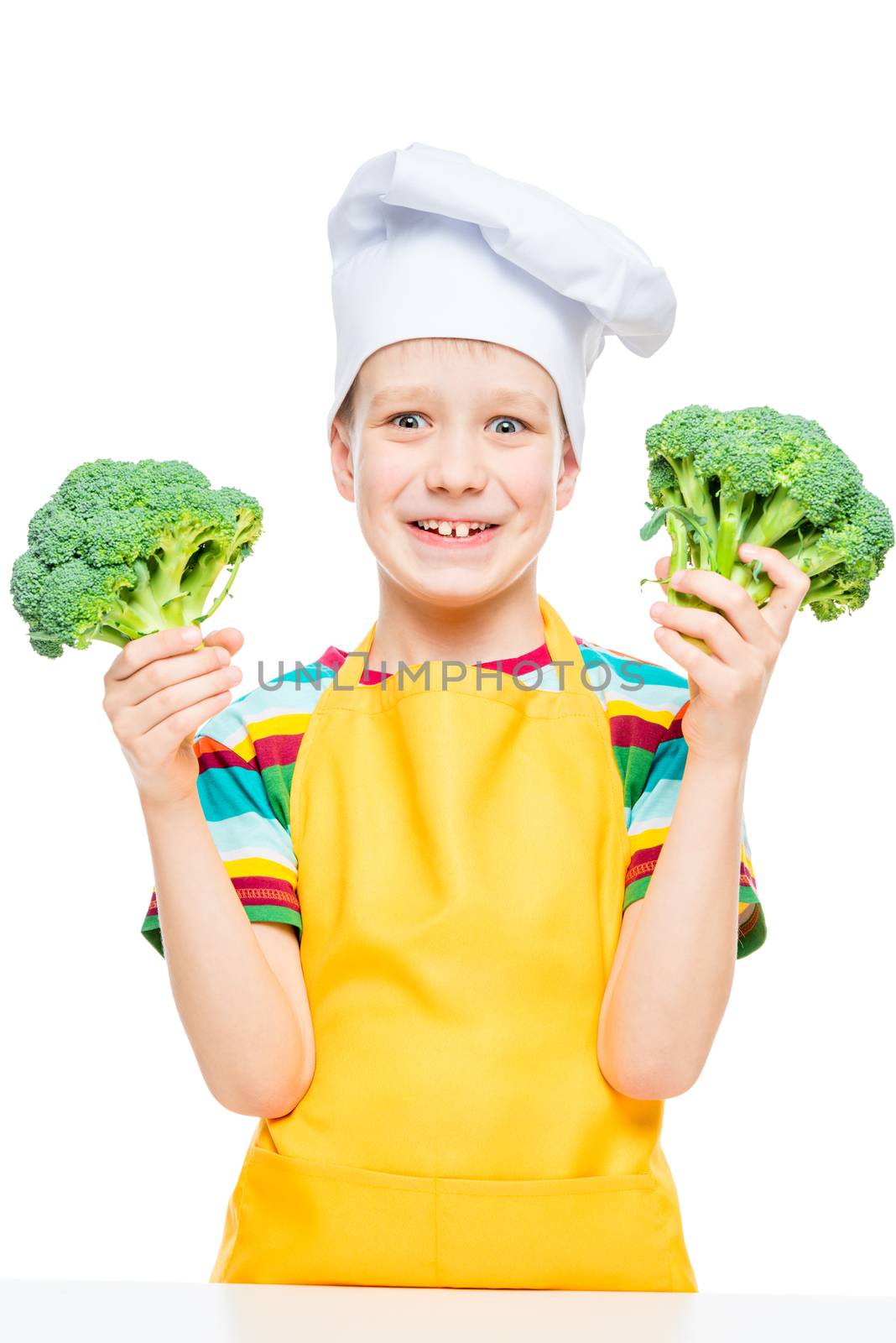 emotional portrait of a boy cook in hat and apron with broccoli on white background isolated