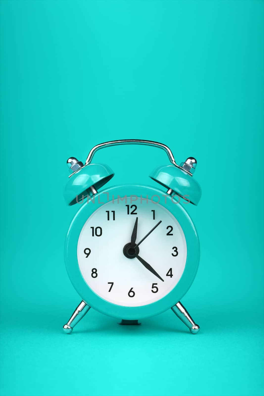 Close up one small teal blue metal twin bell retro alarm clock over aqua turquoise paper background with copy space, low angle front view