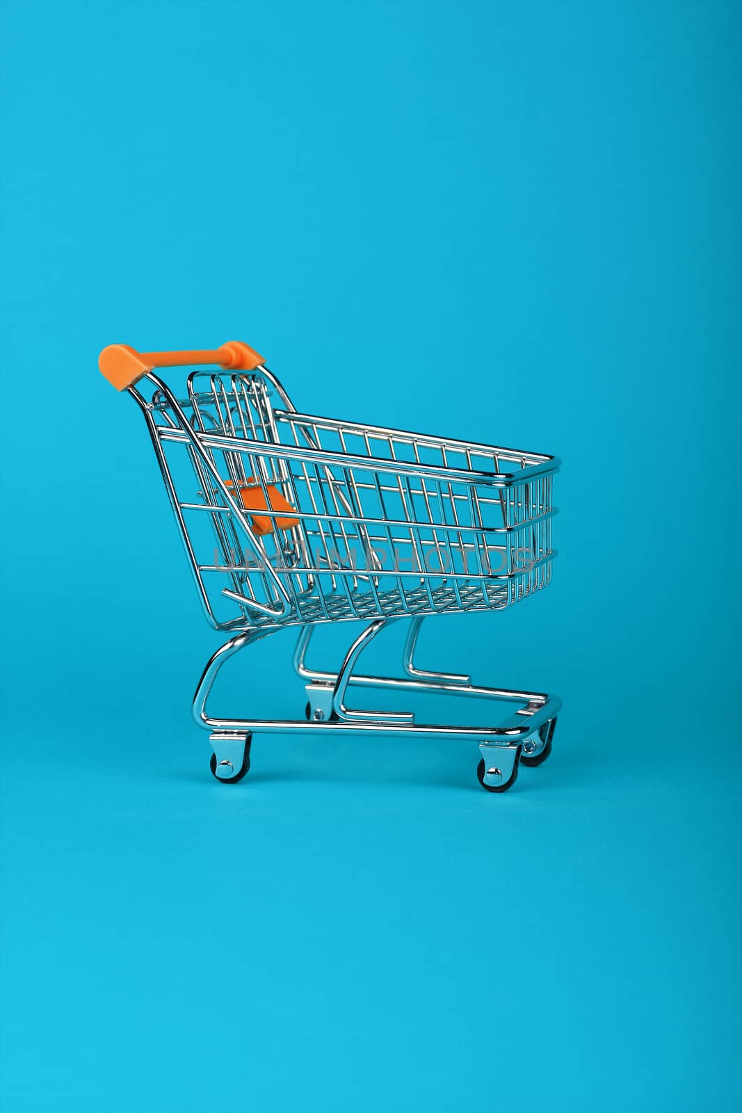 Close up empty toy metal supermarket shopping cart over pastel blue background with copy space, low angle side view