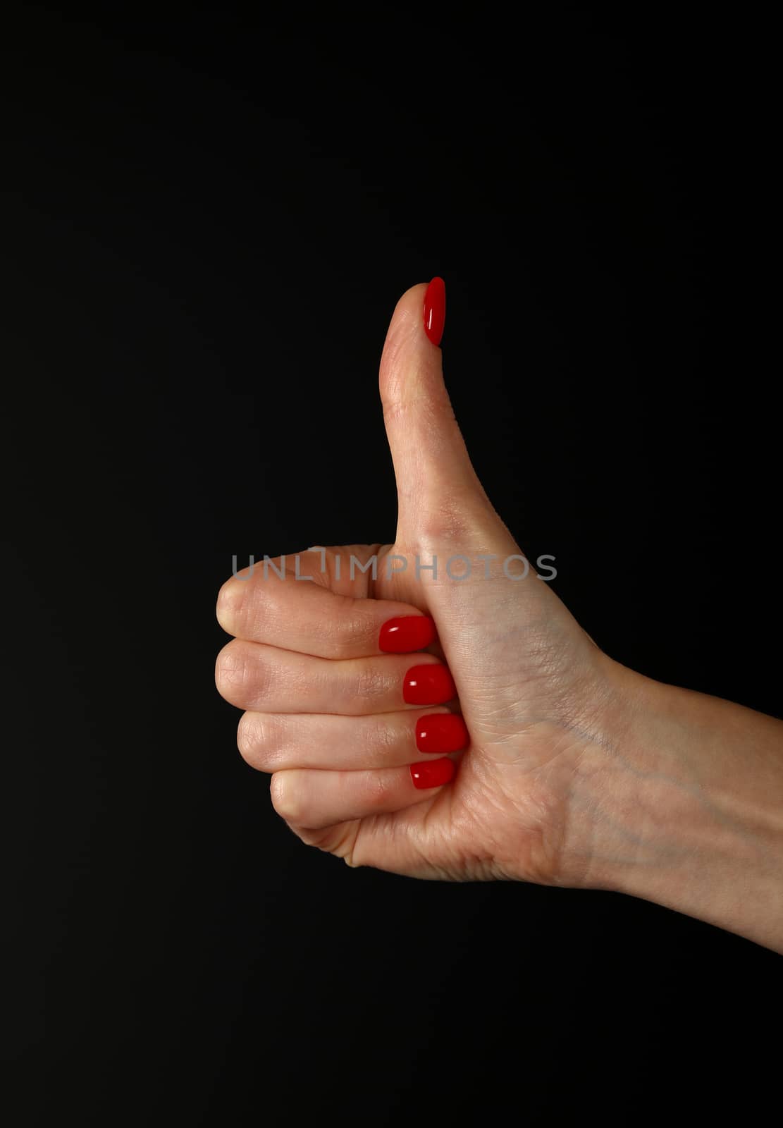 Woman hand with red nails showing thumb up, like, ok or good gesture isolated on black background, side view