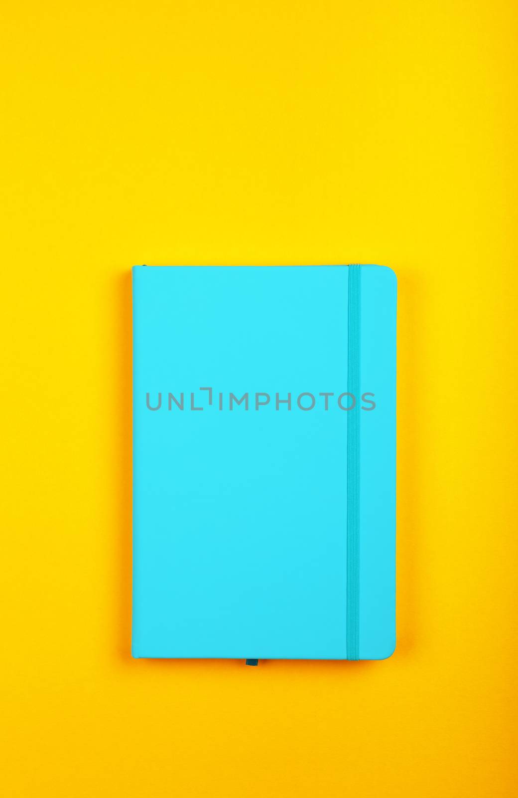 One closed blue faux leather cover notebook on vivid yellow paper background, flat lay, directly above