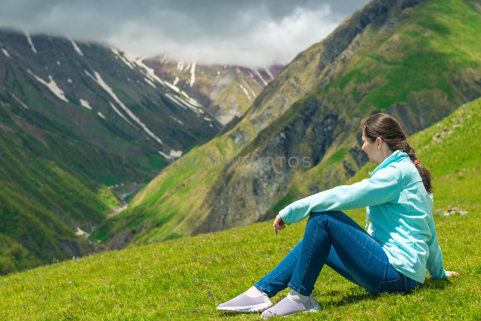 A woman sits on the grass and admires the beautiful mountain landscape in the Caucasus