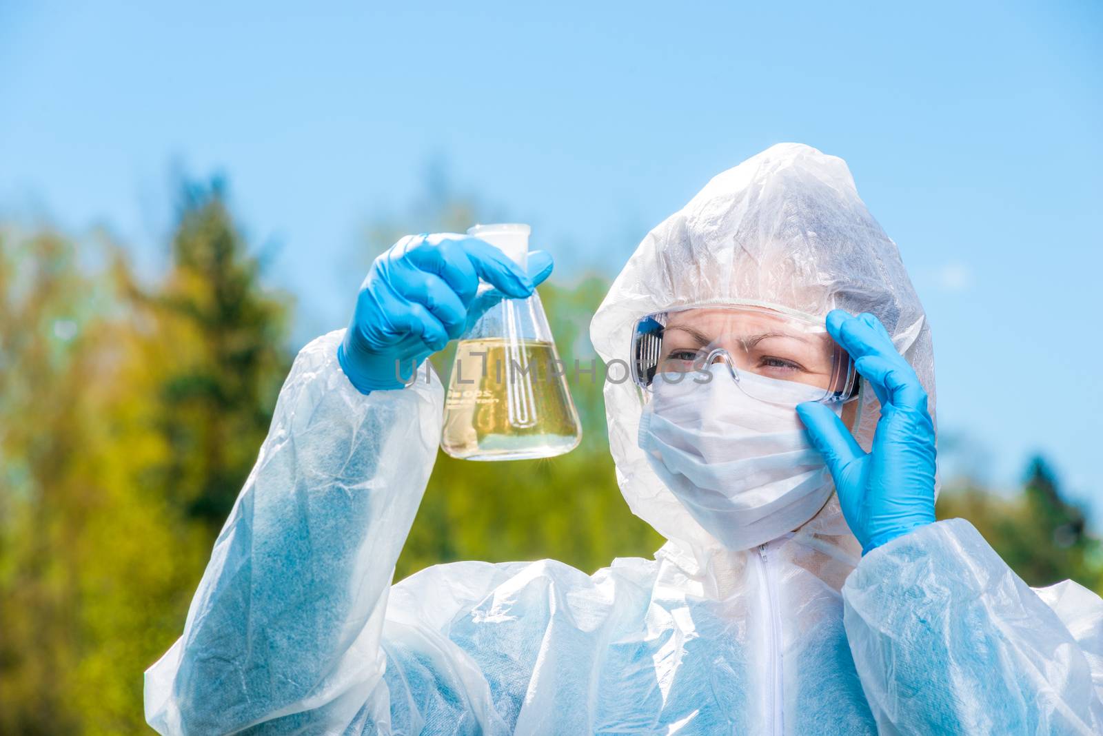 environmental chemist in protective clothing and glasses examines water from a forest lake