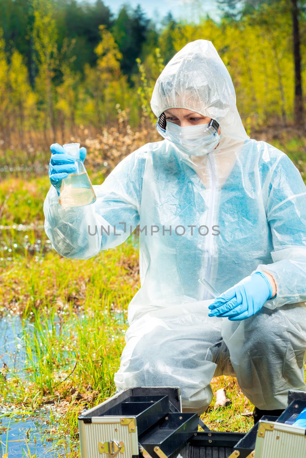 Ecologist with tools and flasks taking water samples from a forest lake for research on dangerous bacteria