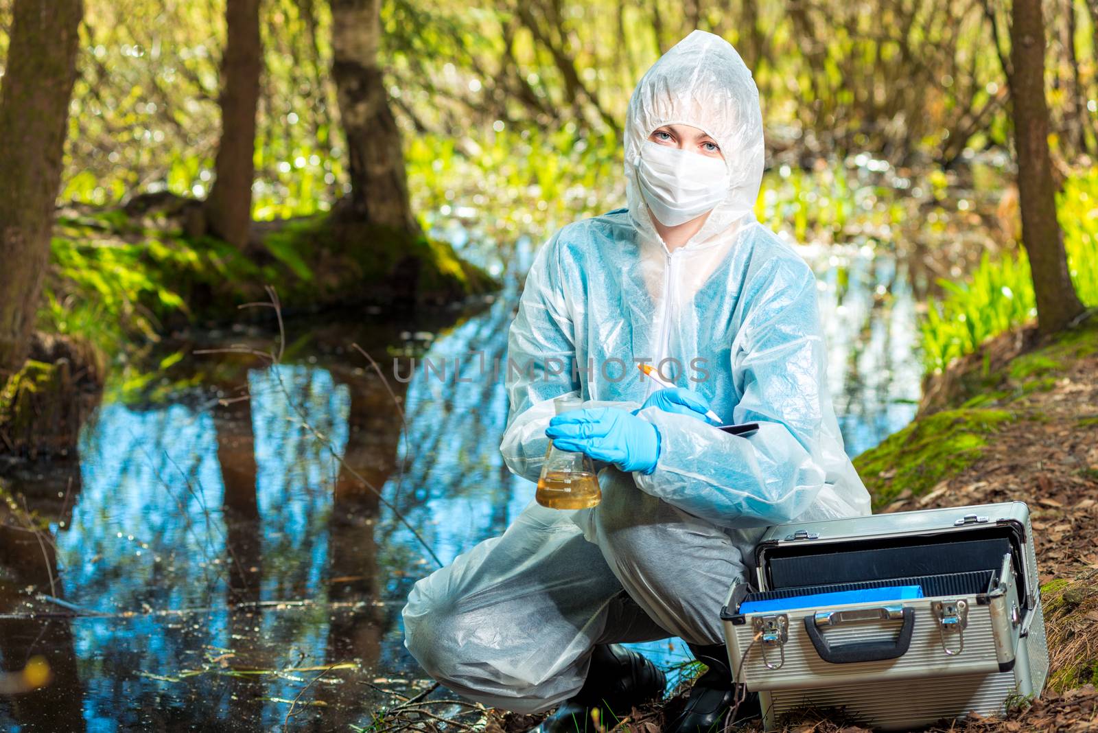 portrait of an ecologist in protective clothing while working, taking water samples from a forest river for analysis