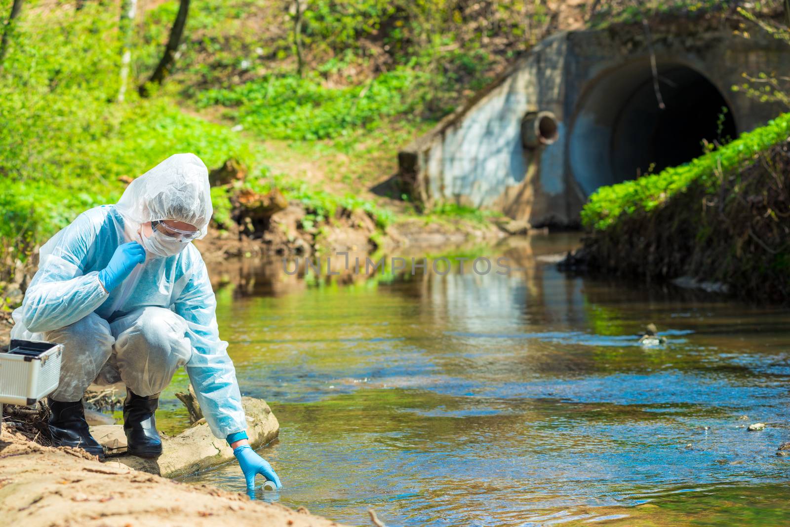 Scientist in protective suite taking water samples from the rive by kosmsos111