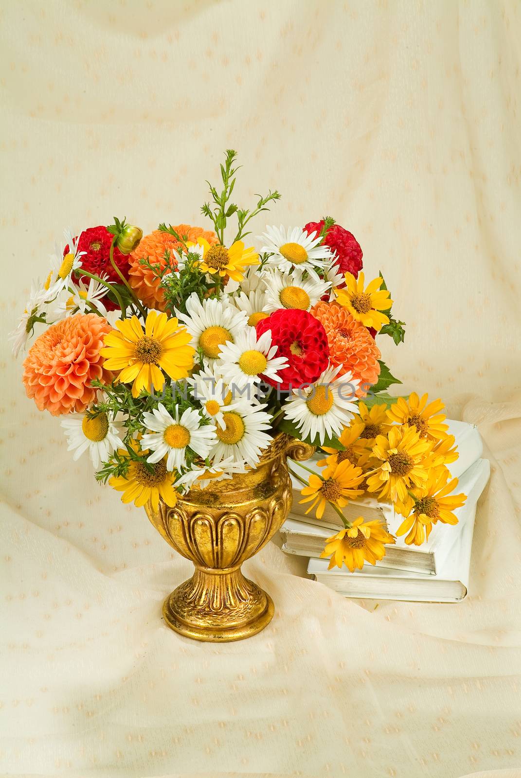 Vase with a bouquet of flowers and books on a fabric background