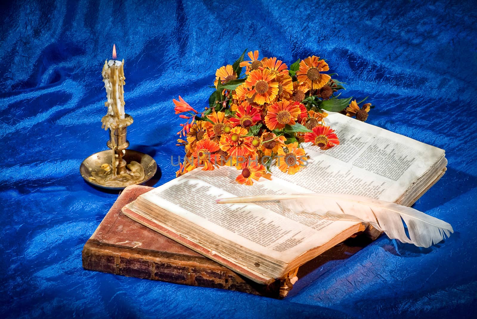 Candle, books and goose feather on fabric background