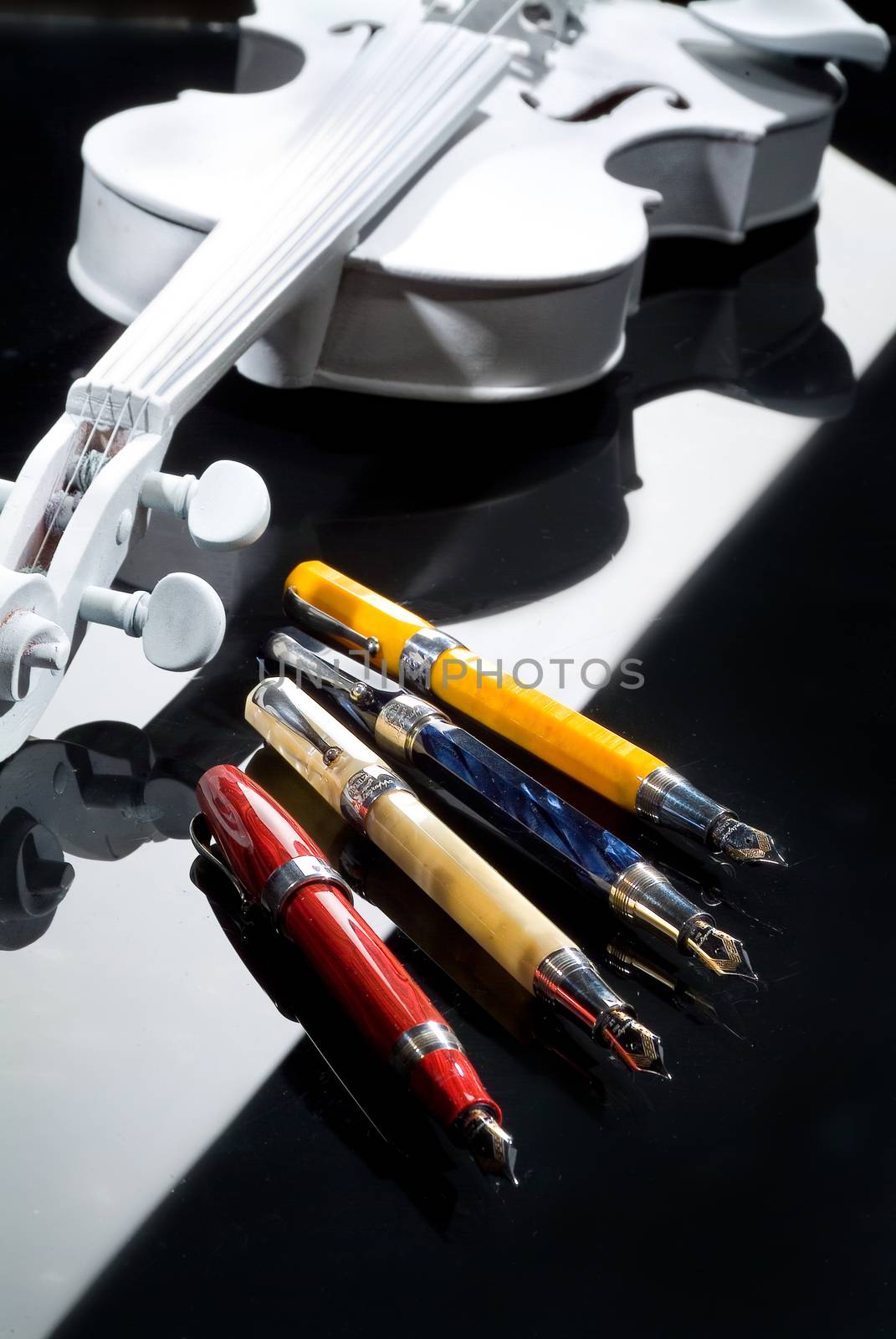 Four different pens and violin on a glass background