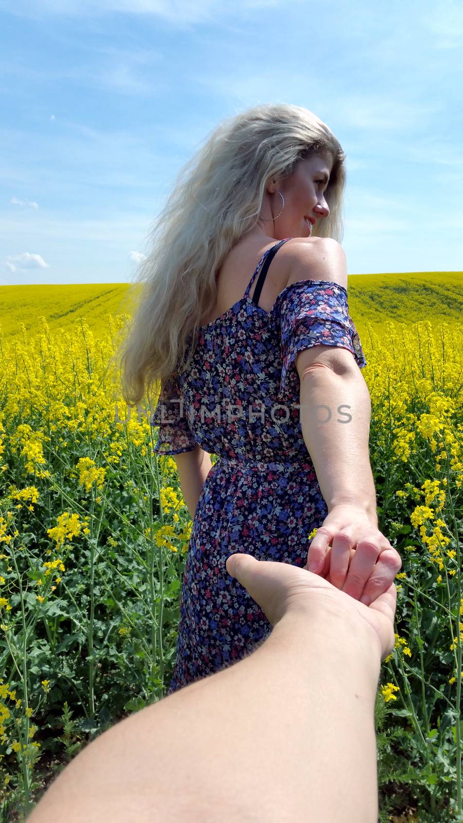 blonde girl in dress with flower print on the blooming yellow rapeseed field