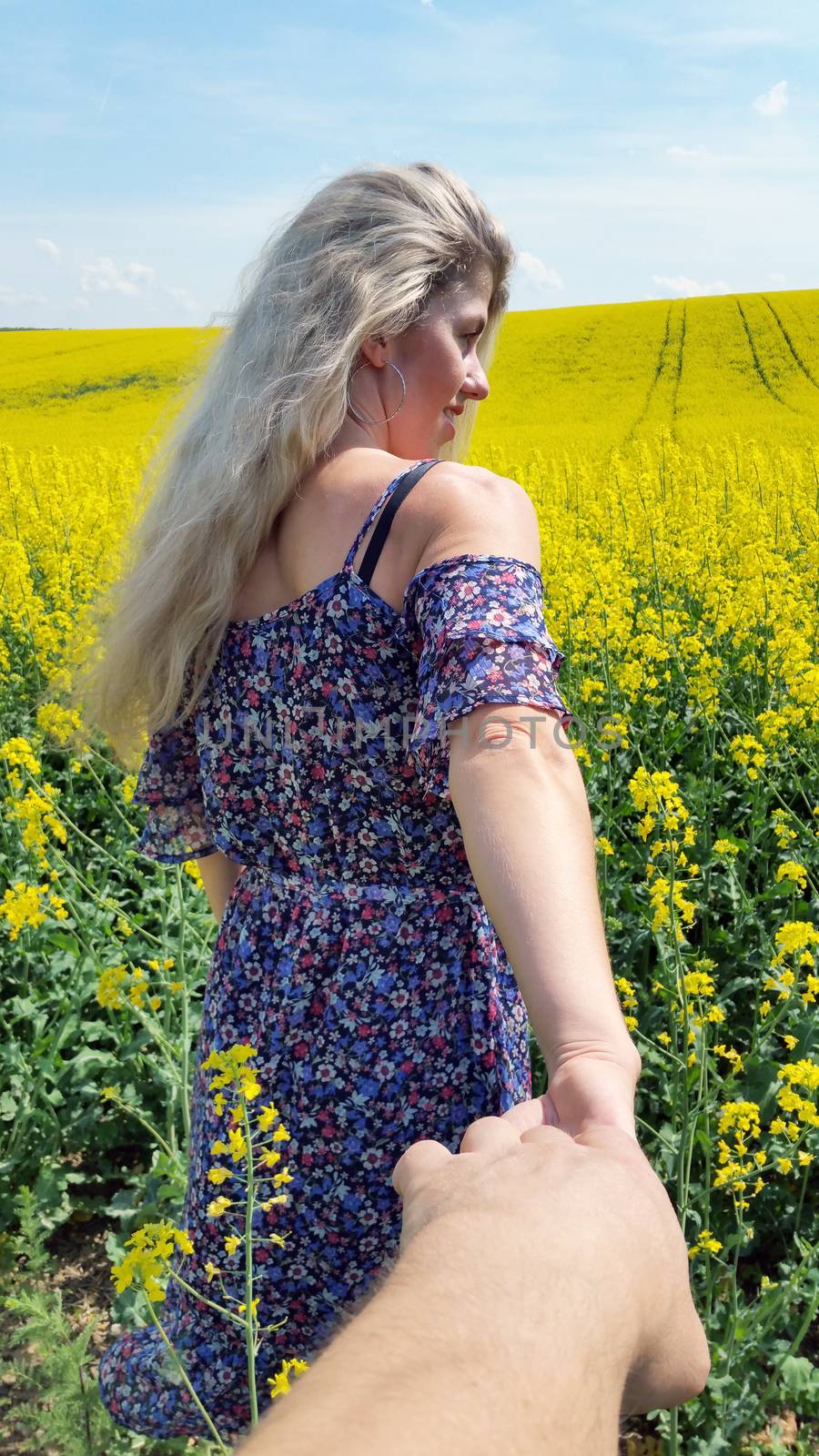 blonde girl in dress with flower print on the blooming yellow rapeseed field