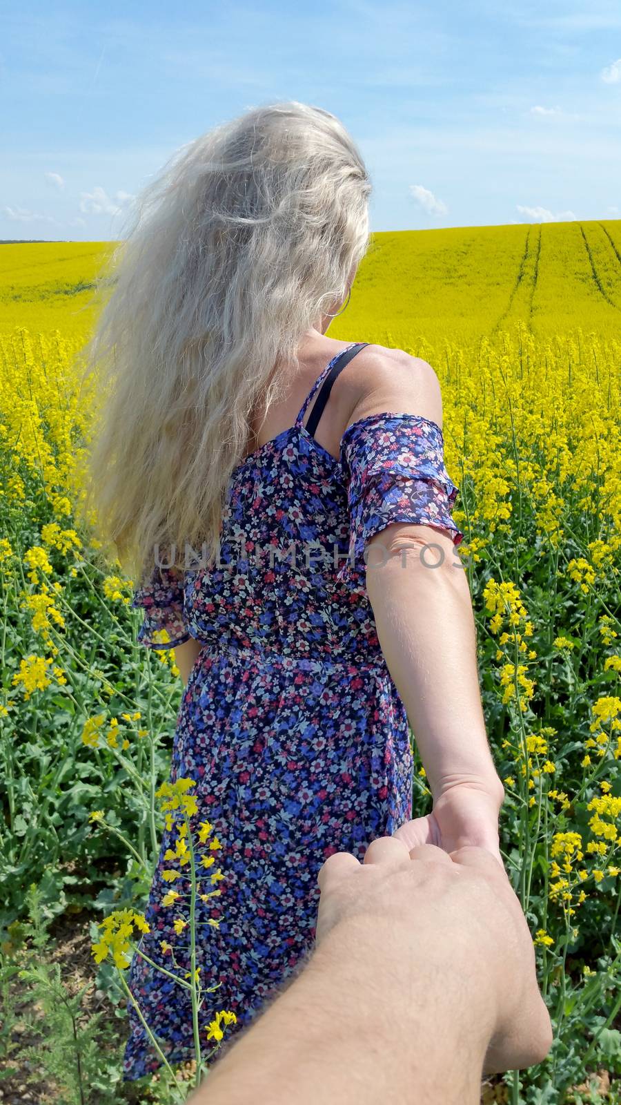 blonde girl in dress with flower print on the blooming yellow rapeseed field