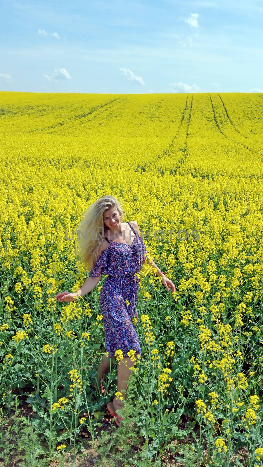 blonde girl in dress with flower print on the blooming yellow rapeseed field