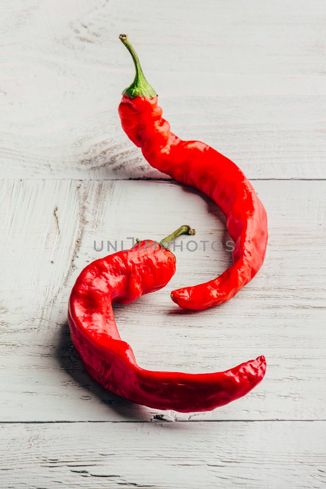 Two ripe chili peppers over white wooden background.