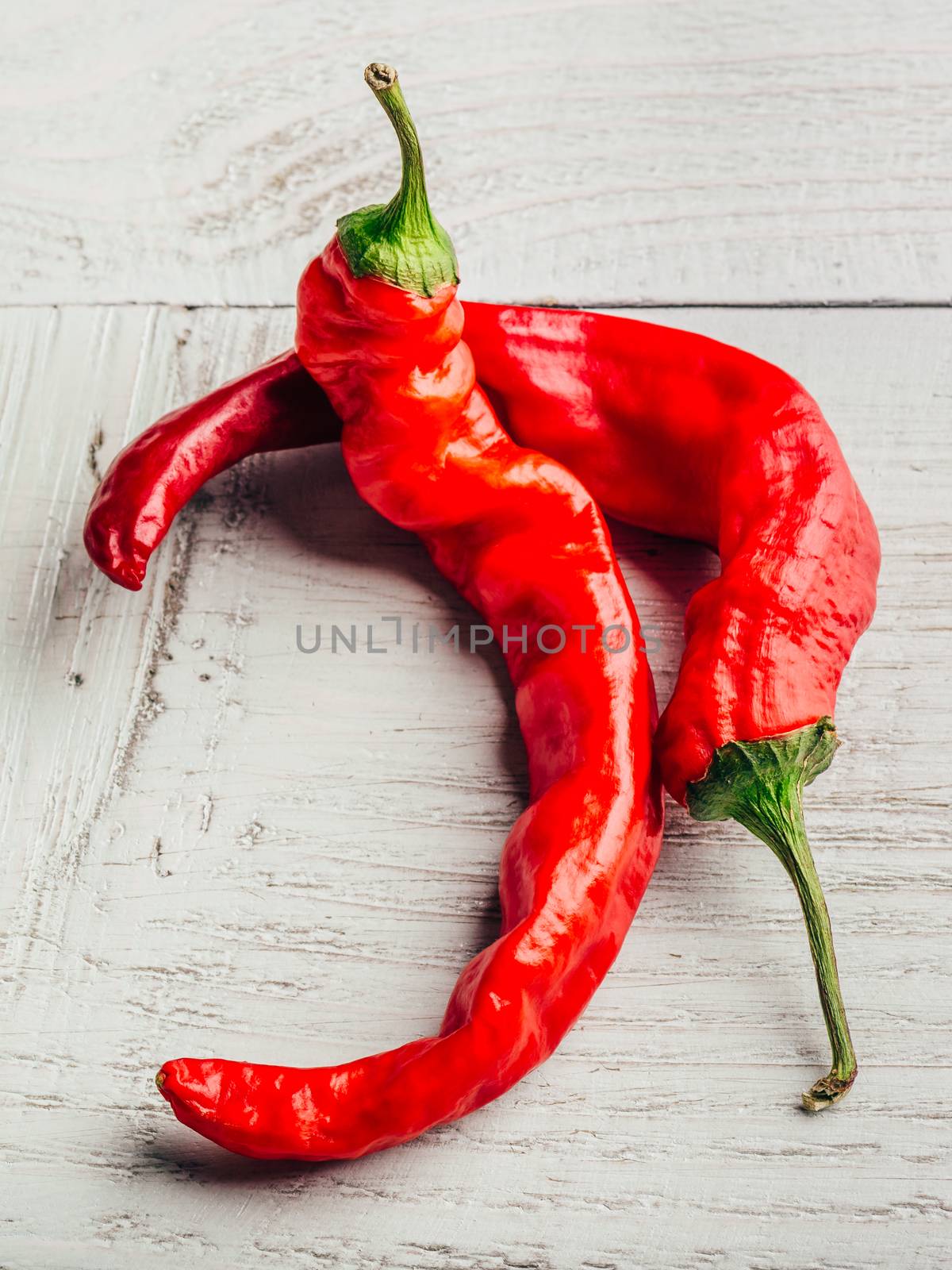 Two fresh chili peppers over white wooden background.