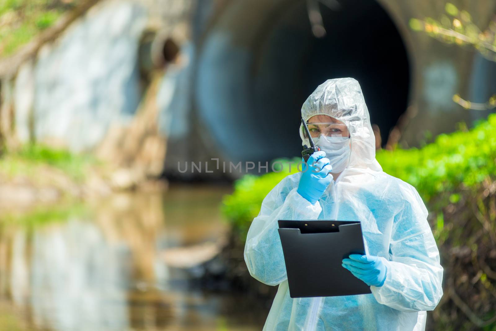 horizontal portrait of a scientist next to a sewer pipe with a walkie-talkie in hand