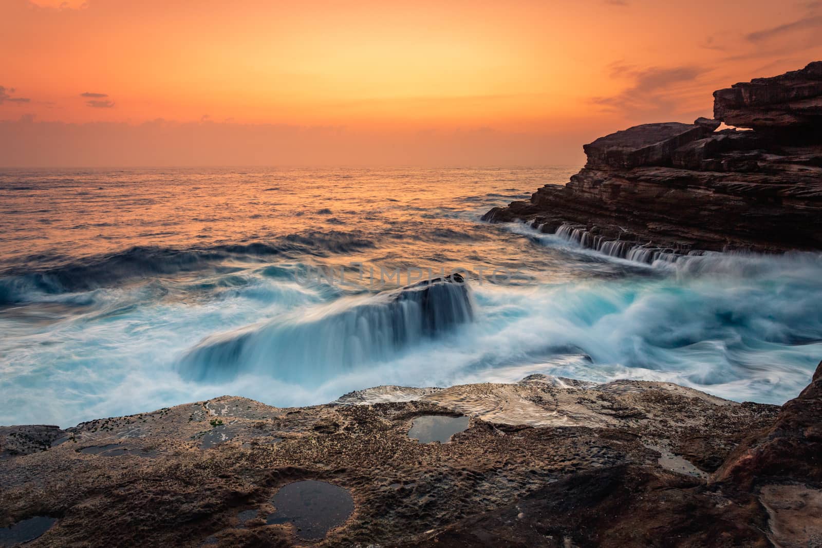Stunning sunrise on the Sydney sea coast and beautiful motion flows across shipwreck rock as waves crash and tumble over it and onto the rock shelf and headland.