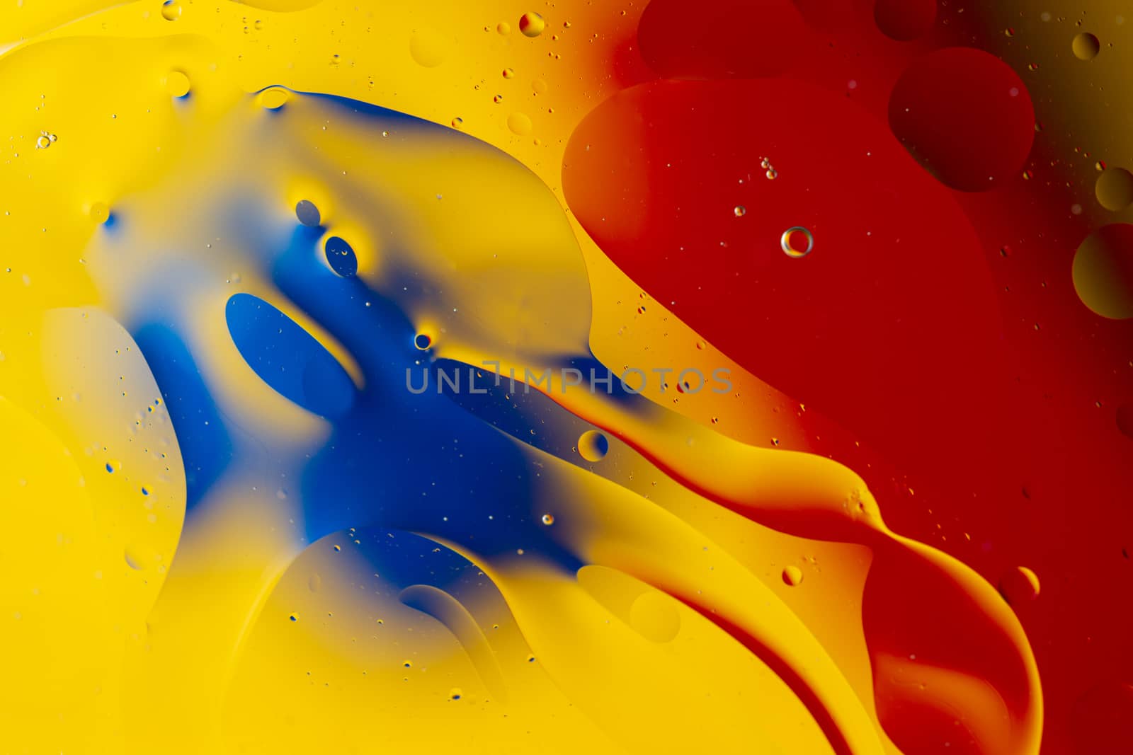 Abstract oil spots in motion on water on blurred yellow background. Red and blue spots on blurred background. Photo with small depth of field.