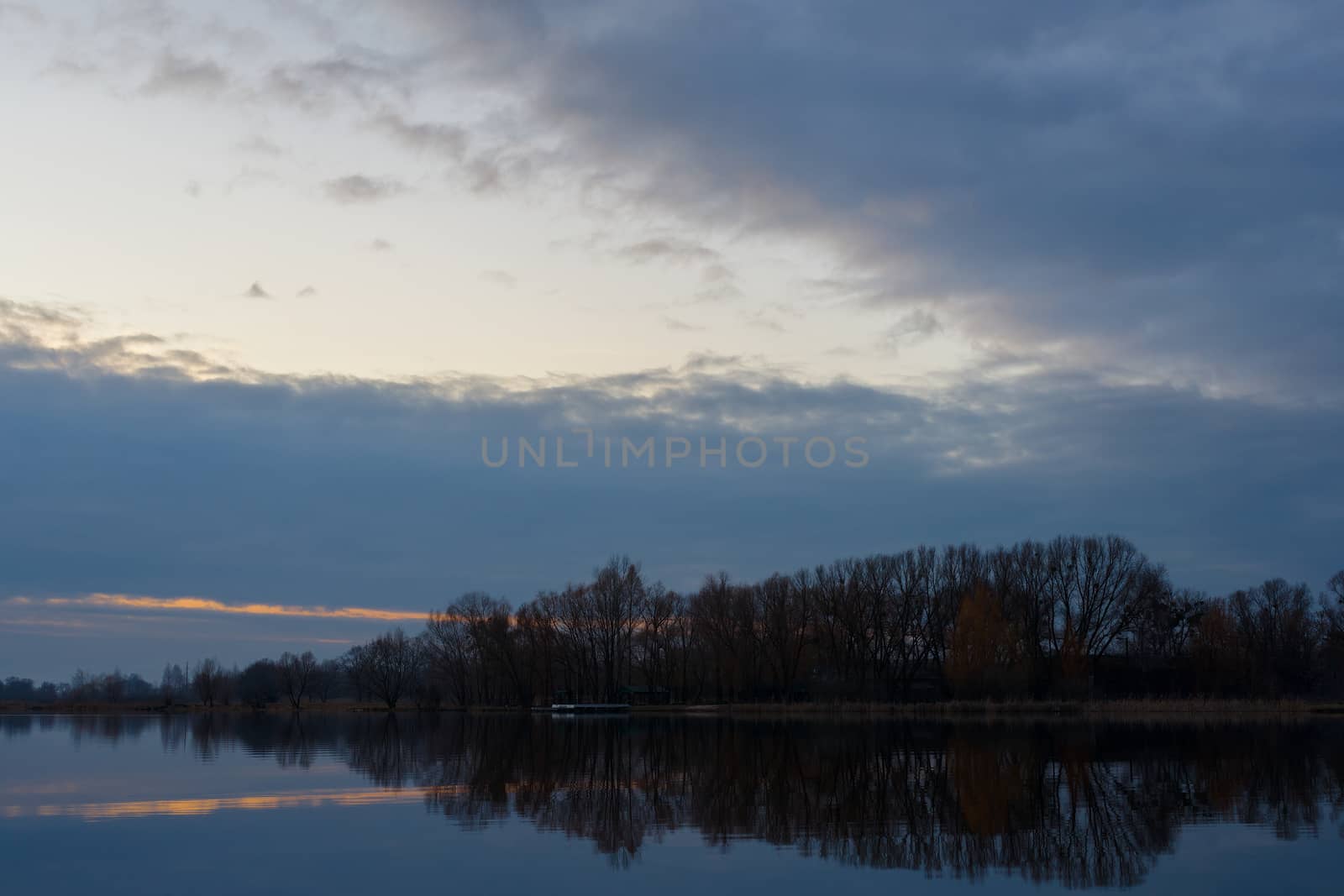 Gray evening sunset above the lake or river. Blue clouds on horizon