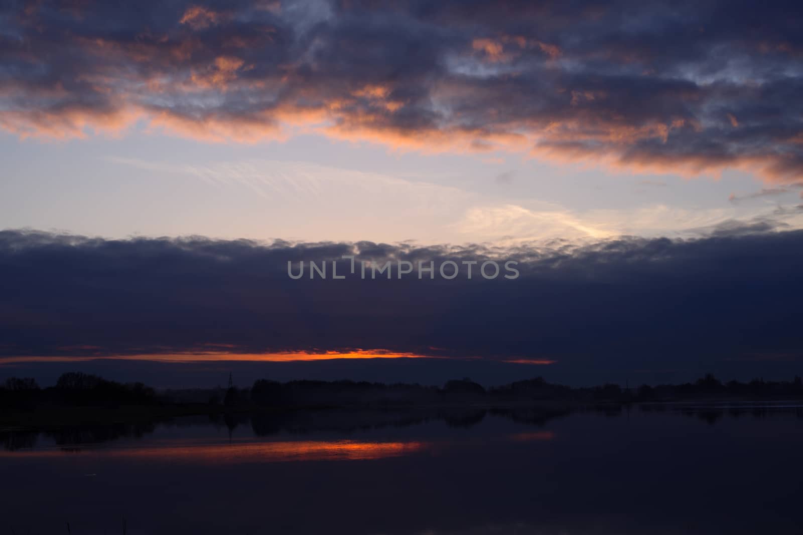 Red evening sunset above the lake or river. Purple and blue clouds and falling sun