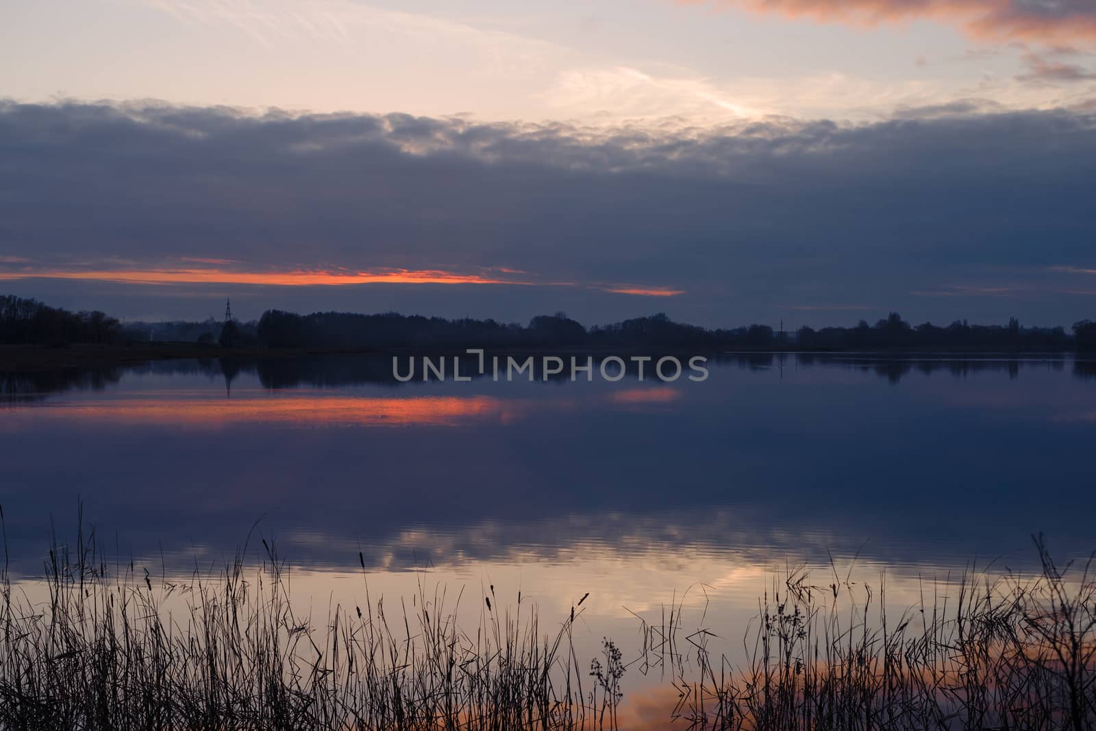 Red evening sunset above the lake or river. Purple and blue clouds and falling sun