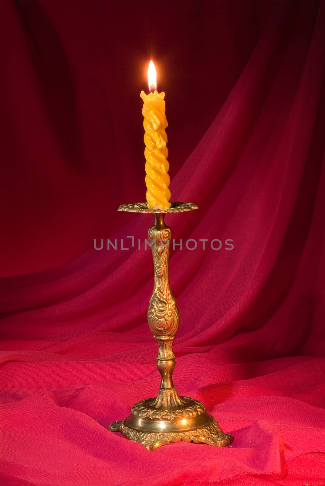 Candle in a stick on a red fabric studio background