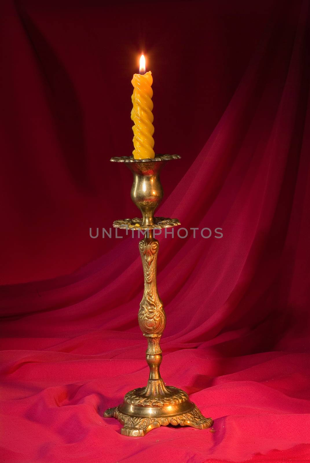 Candle in a stick on a red fabric studio background