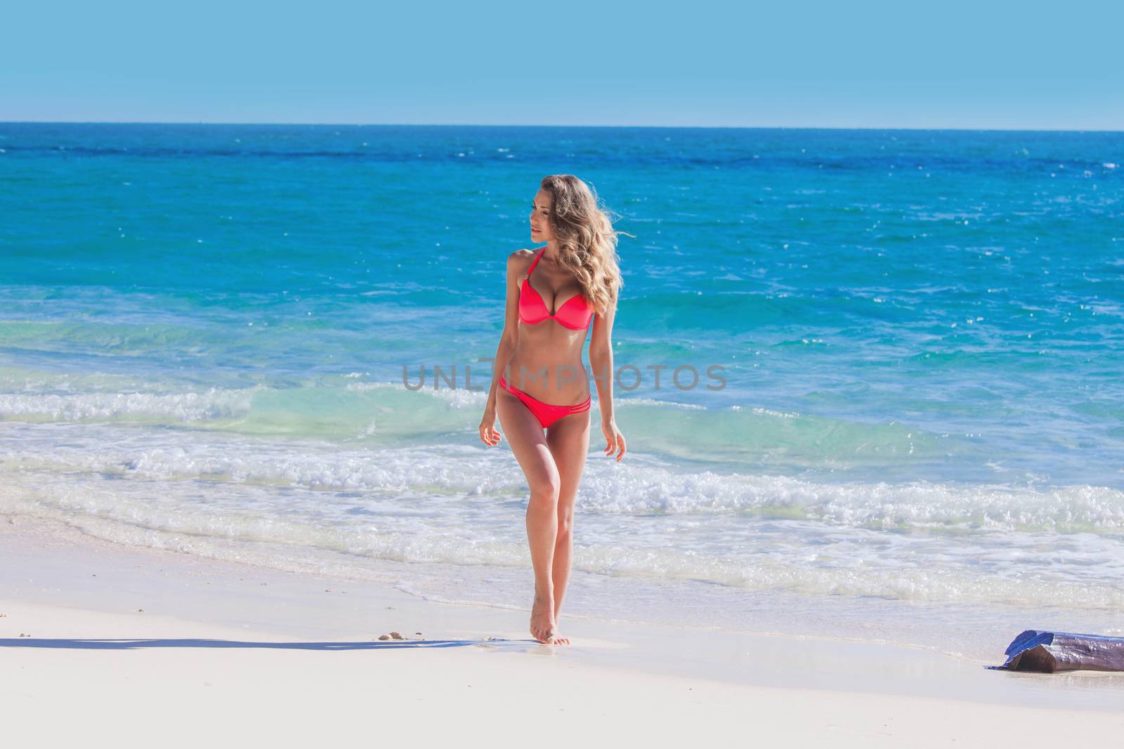 Happy tanned girl in red bikini at seaside, blue sea water in background