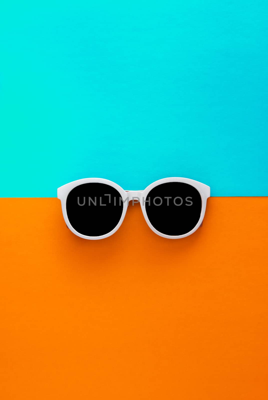 Sunny stylish white sunglasses on a bright blue-cyan and yellow-orange background, top view, isolated. Copy space. Flat lay by Tanacha