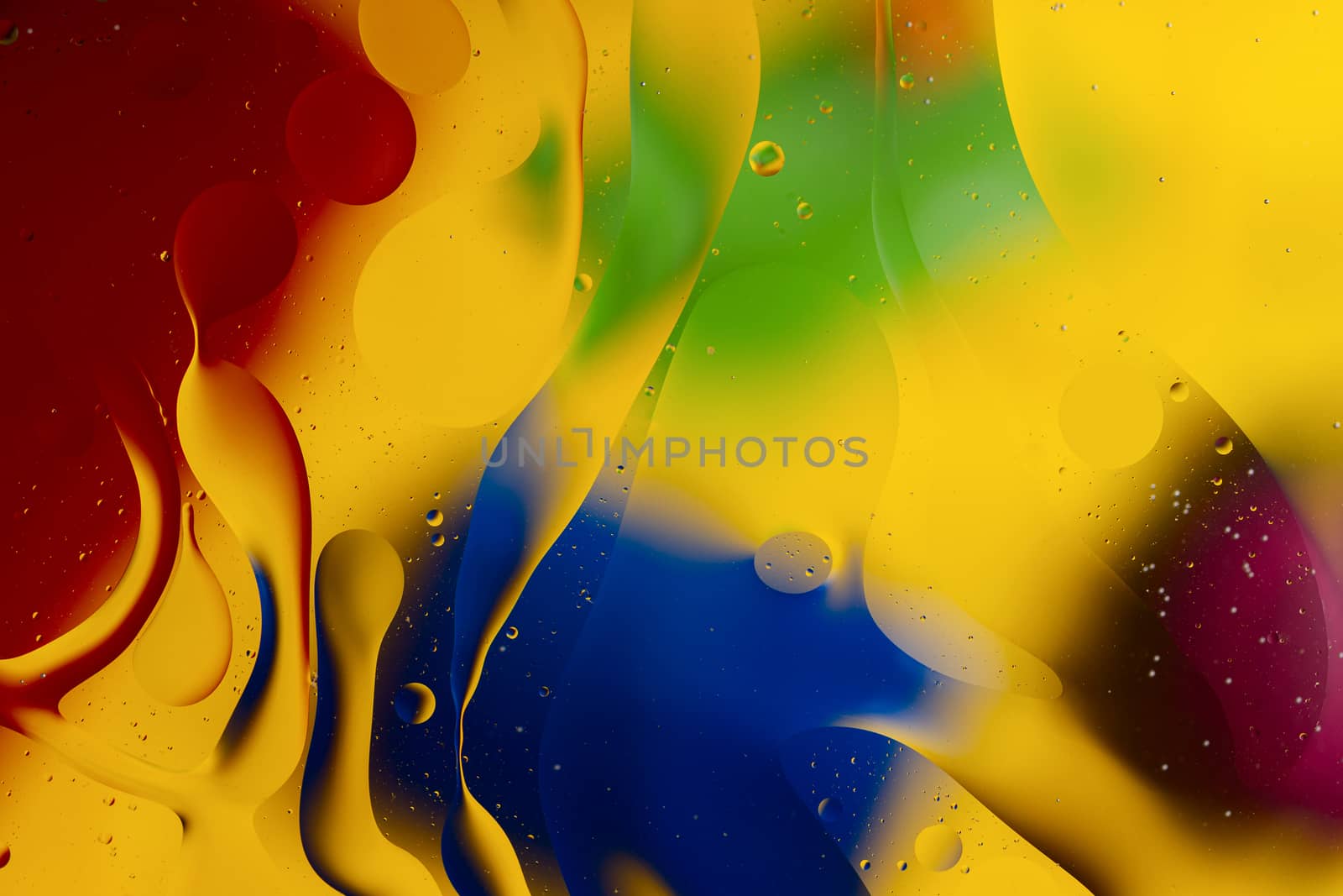 Abstract oil spots in motion on water on blurred yellow background. Red, green, purplee and blue spots on blurred background. Photo with small depth of field.