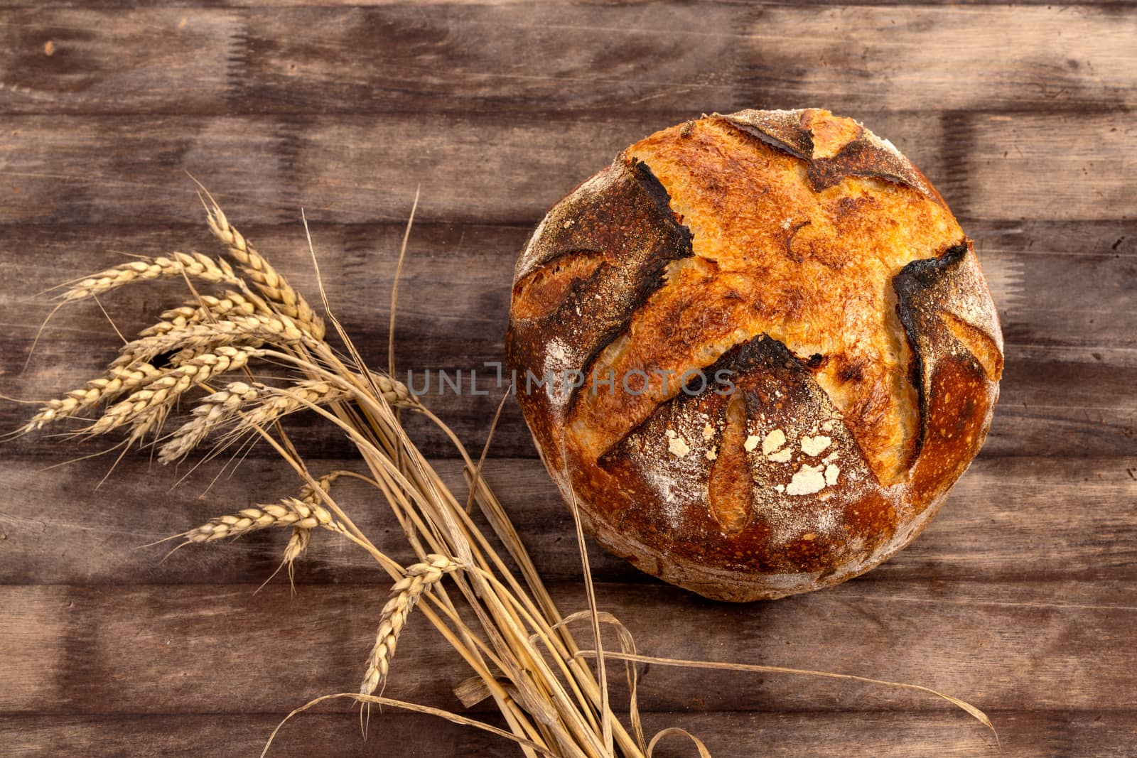 Freshly baked artisan sourdough bread loaf with wheat grains on a wooden board.