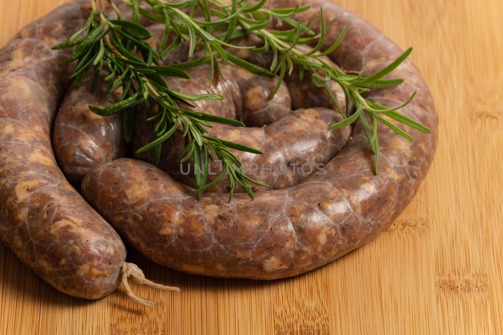 Raw homemade stuffed pork sausages and rosmarin isolated on a wood board.