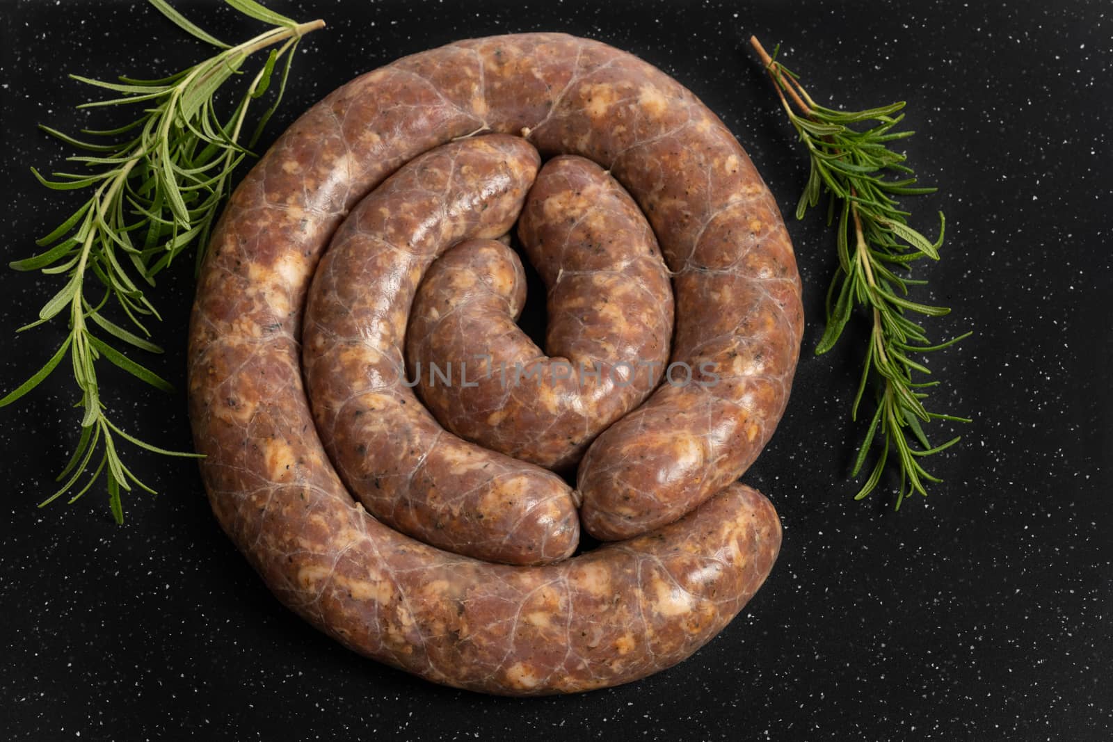 Raw homemade stuffed pork sausages and rosmarin isolated on a black background.