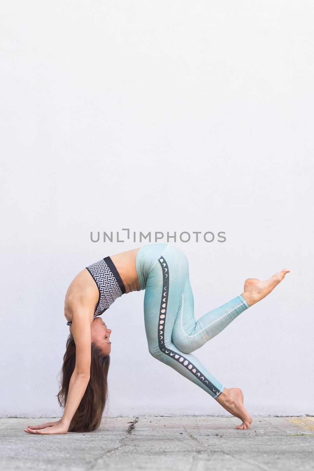 Fit sporty active girl in fashion sportswear doing yoga fitness exercise in front of gray wall, outdoor sports, urban style.