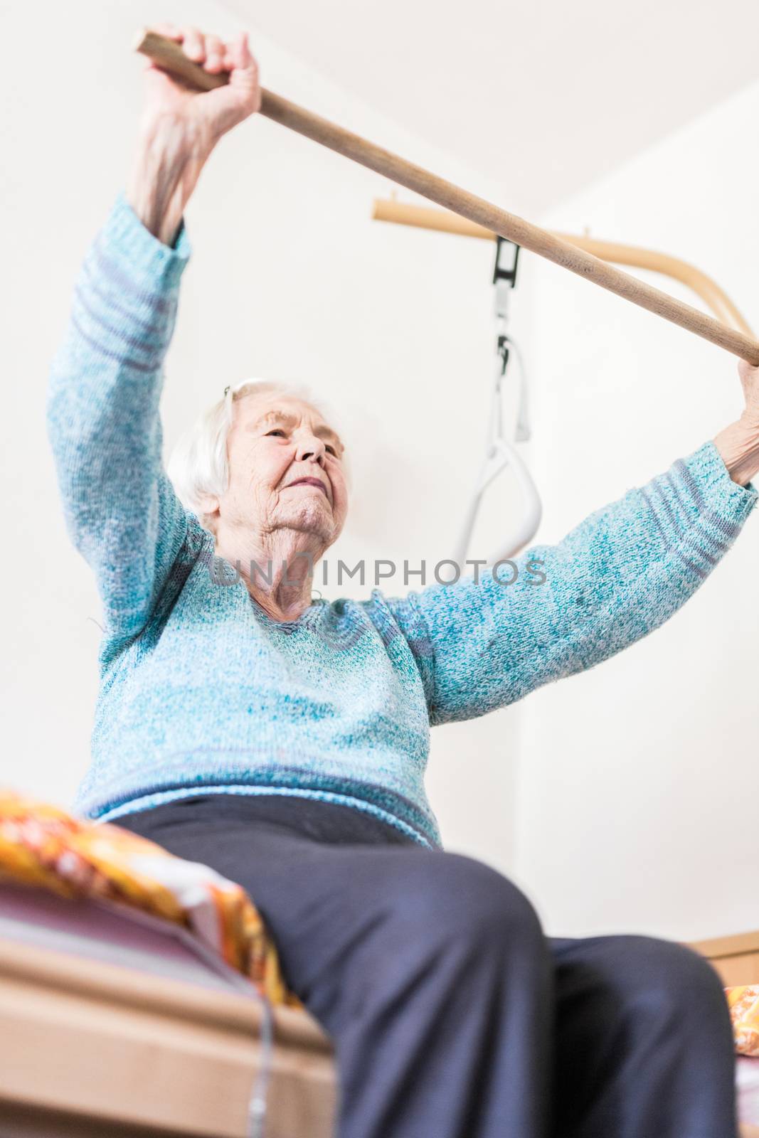 Elderly 96 years old woman exercising with a stick sitting on her bad. Geriatric health care home assisted support for older people concept. Care for the elderly.