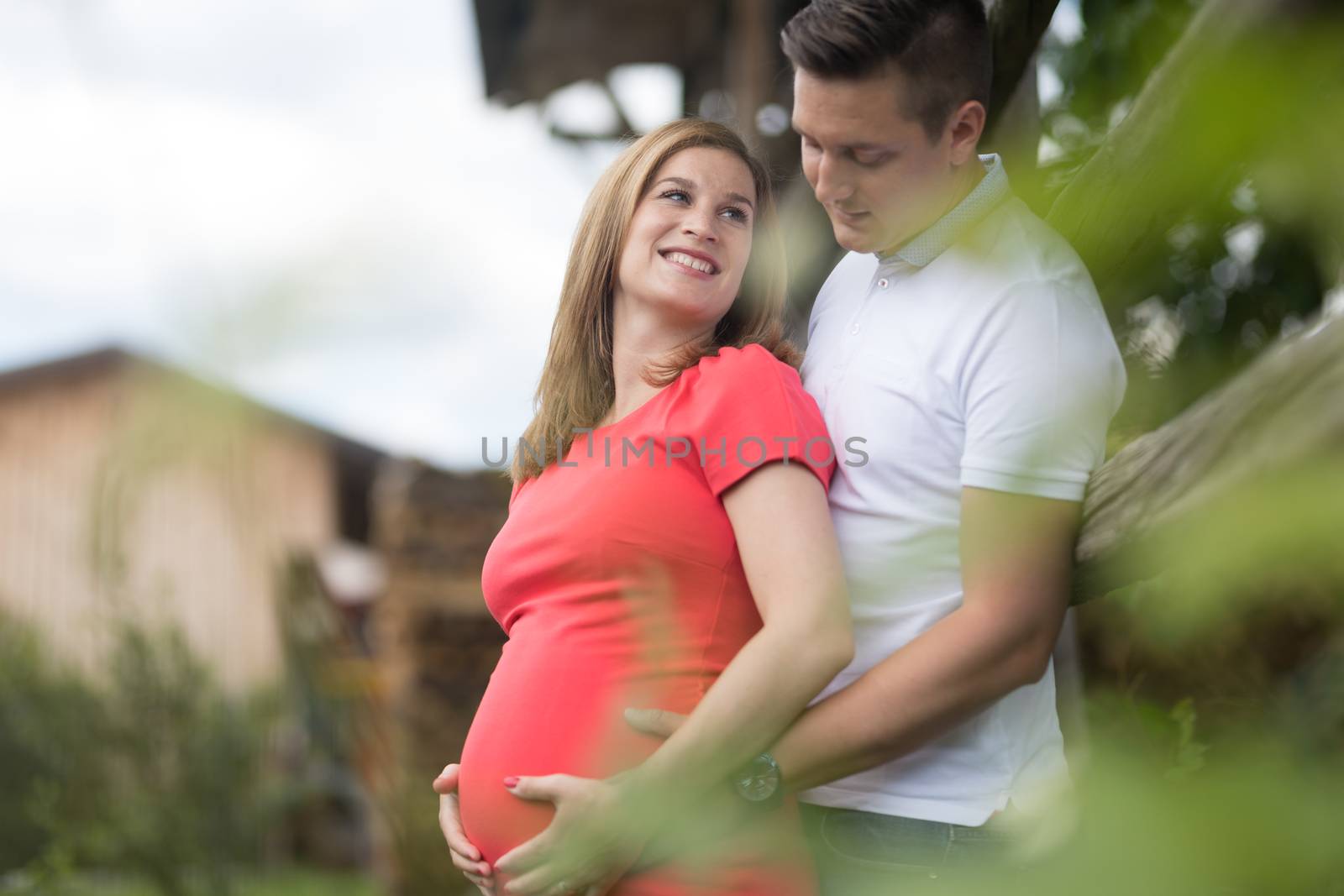 Young happy pregnant couple hugging by hayrack in a vineyard. Concept of love, relationship, care, marriage, family creation, pregnancy, parenting